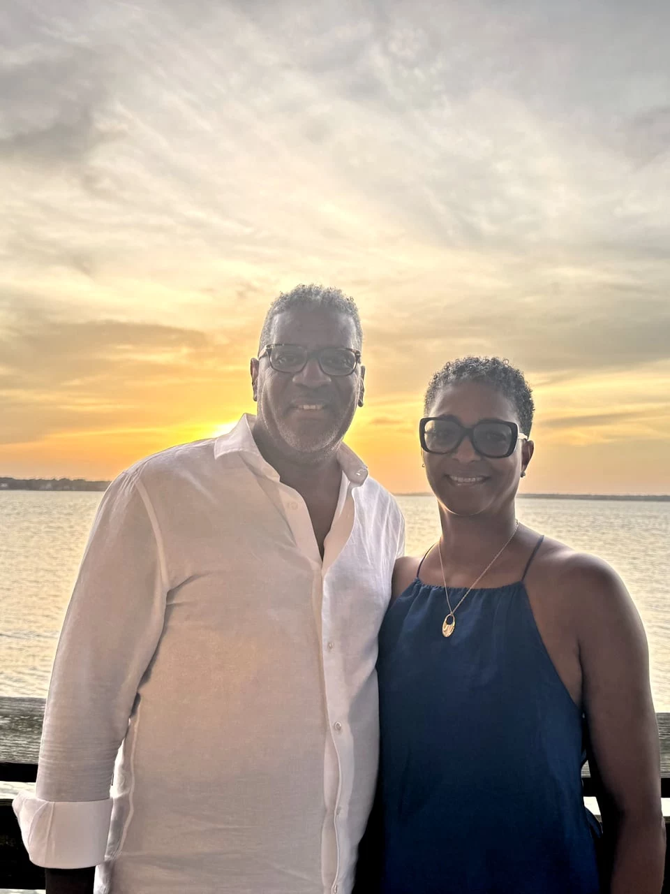 Smiling couple standing together by the water at sunset