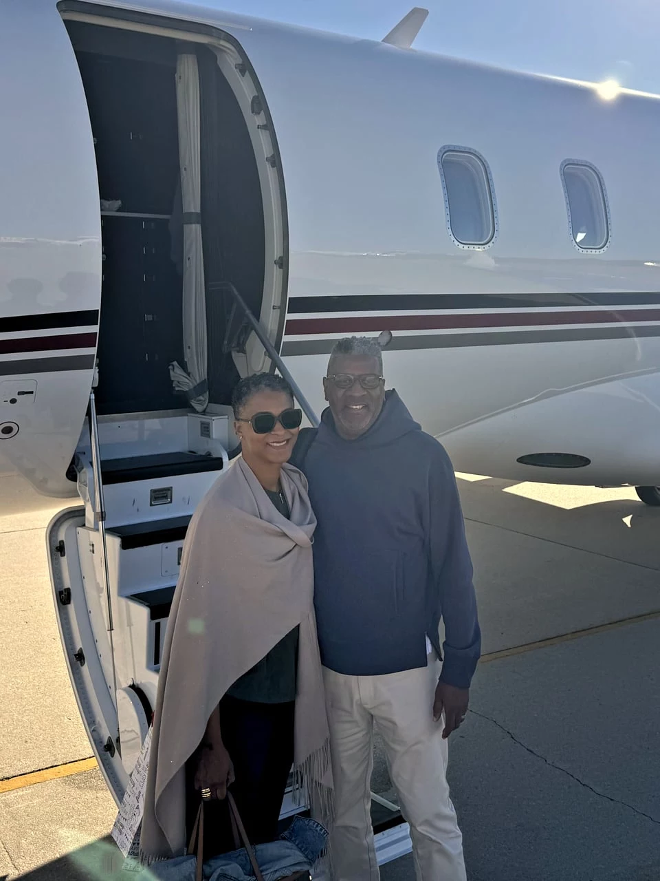 Smiling couple standing beside a private jet on the tarmac